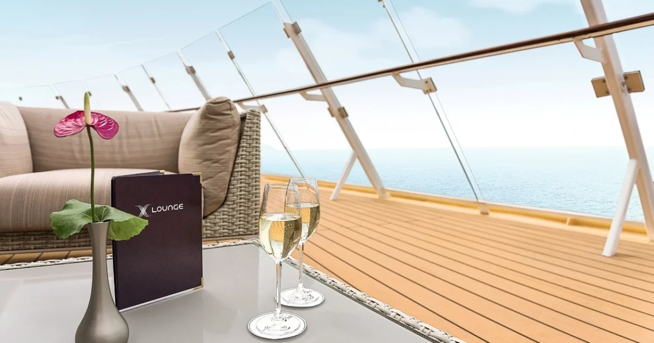 Loungesessel und Tisch mit Karte und zwei Sektgläsern im Außenbereich der X-Lounge auf Mein Schiff 4 mit Blick aufs Meer