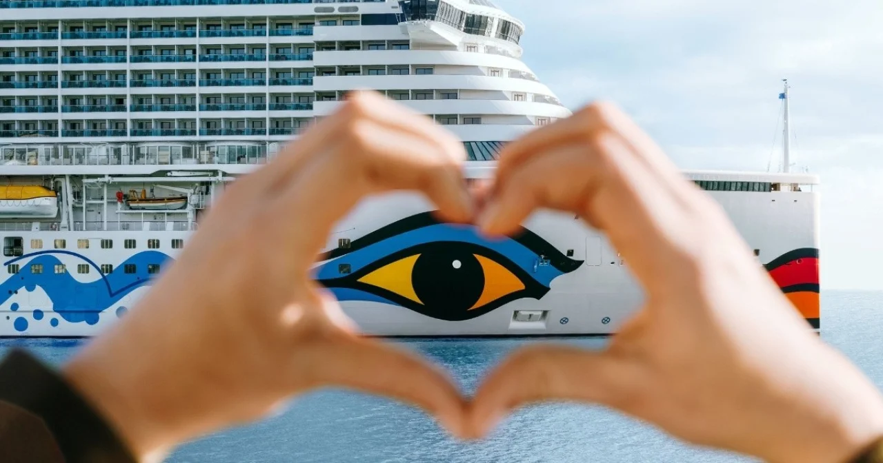 Hand formt Herz vor AIDA Kreuzfahrtschiff mit Bugbemalung mit Auge und lächelndem Kussmund