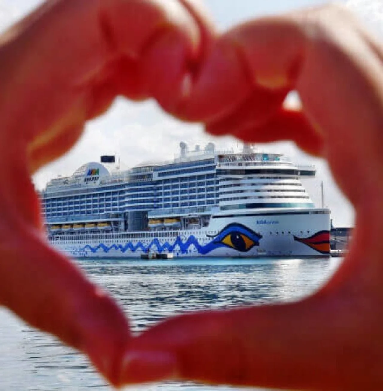 Herz formende Hand vor AIDA Schiff
